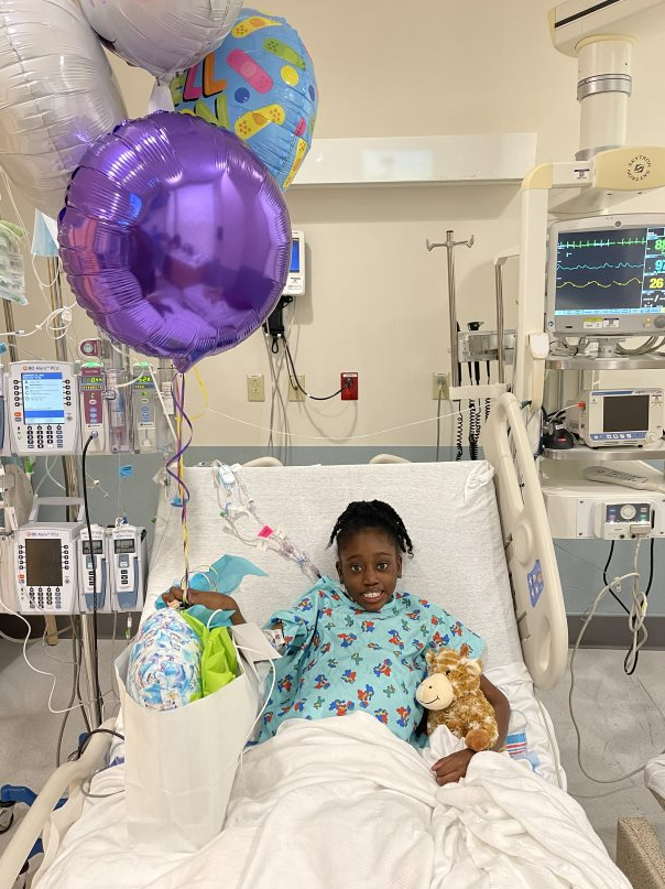 Bra’laya smiles in a hospital bed surrounded by balloons and gifts.