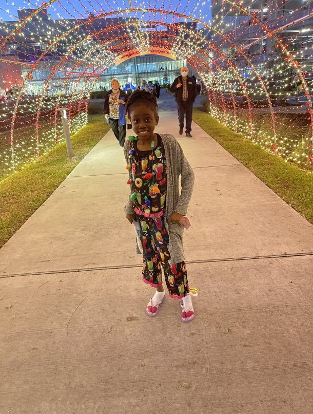 Bra'laya smiles brightly while standing under a festive light tunnel.