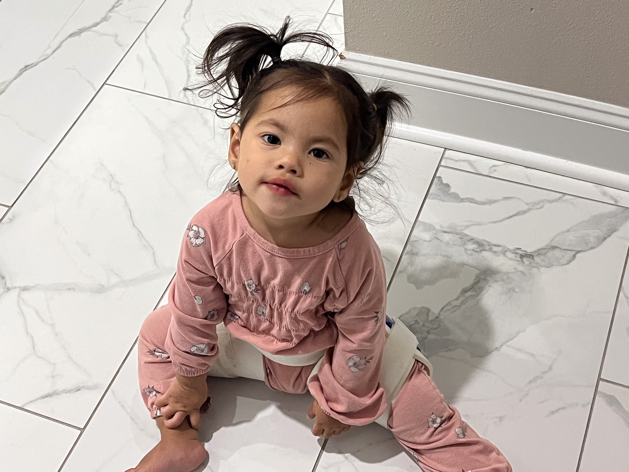 Selena in a pink outfit sits on a marble floor.