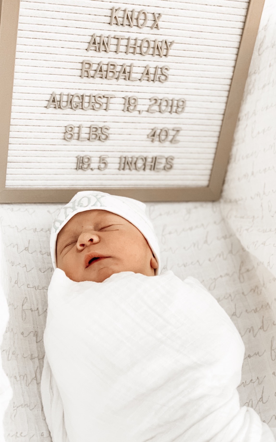 Baby Knox is swaddled in white, lying next to a letter board announcing his birth information.